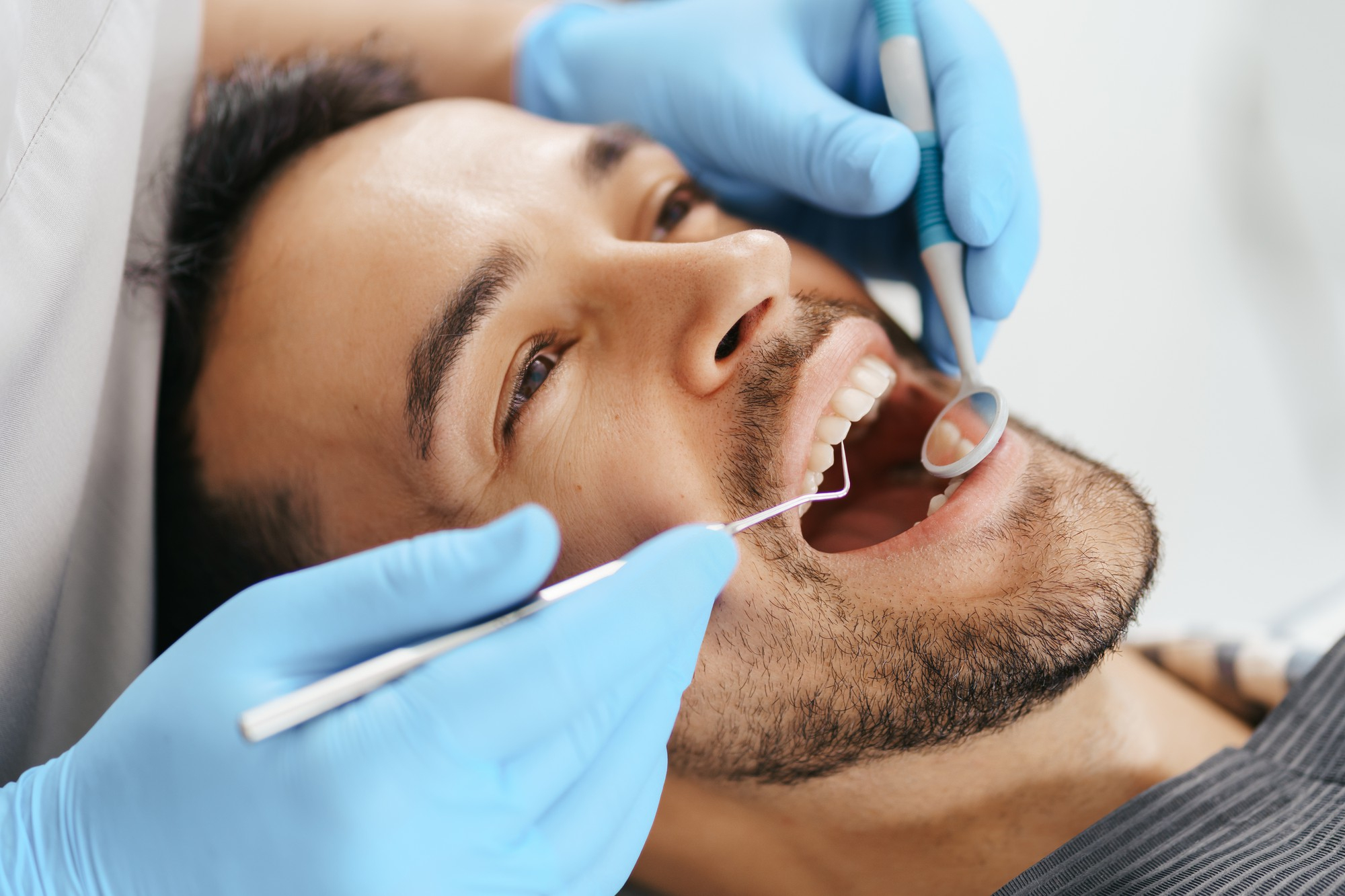 sonriente-joven-sentado-silla-dentista-mientras-medico-examina-sus-dientes
